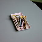 Het HK Living 70s Ceramics Serveerschaaltje Muse bevat verschillende kleurrijke, gespikkelde lepels, allemaal uitgestald op een glad, lichtgrijs oppervlak.