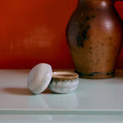 De HK Living 70s Ceramics Suikerpot Petal - een suikerpot van keramiek - staat op een licht oppervlak, met een grote bruine vaas erachter die afsteekt tegen een warm oranje muur, en weerspiegelt de retro charme van de iconische stijl van HK Living.