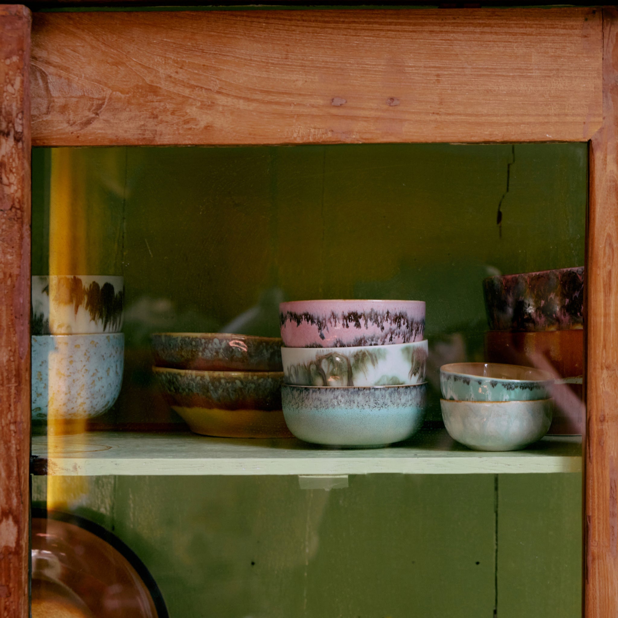 Het HK Living 70s Ceramics Tapasschaaltje Renaissance 4 st. kommen in levendige retro designs staan op een lichtgroene plank en voegen vintage flair toe aan de houten vitrinekast.