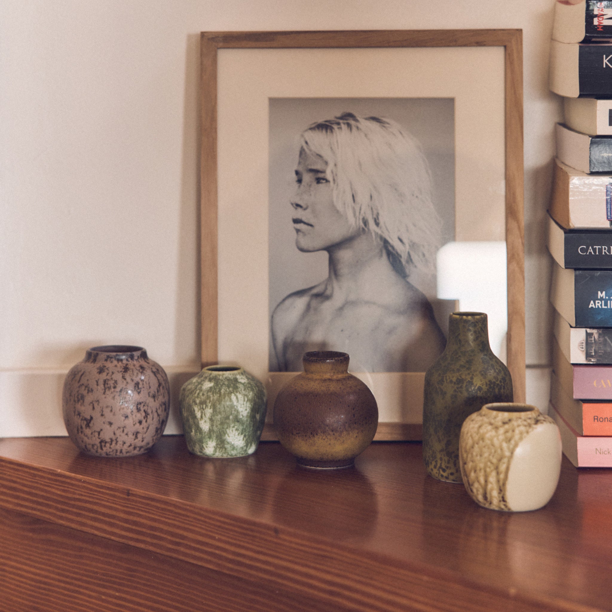 Een ingelijst zwart-wit portret ligt op hout, omringd door HK Living 70s Ceramics Vaasjes Pursuit 5 st. en een stapel kleurrijke boeken - ideaal voor fans van retro interieurdecoratie.