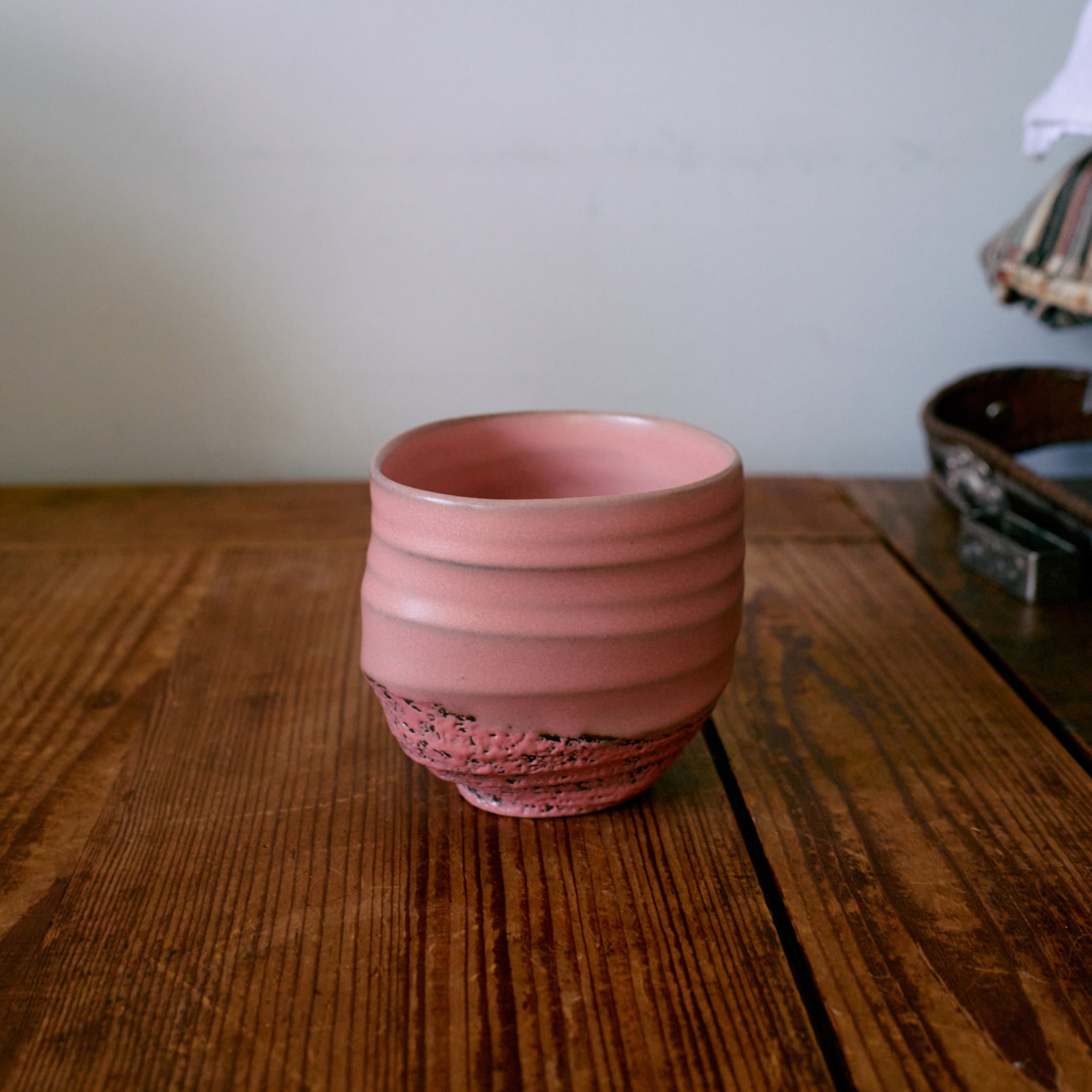 Een set van vier HK Living Artist Ceramics koffiekoppen in roze met een gestructureerde basis rust op een houten tafel, met een effen achtergrond en een deel van een tas zichtbaar aan de rechterkant.