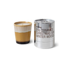 Een kaars van geel en crème keramiek staat naast een glanzend zilveren HK Living Christmas Special Geurkaars Winter Woods houder.