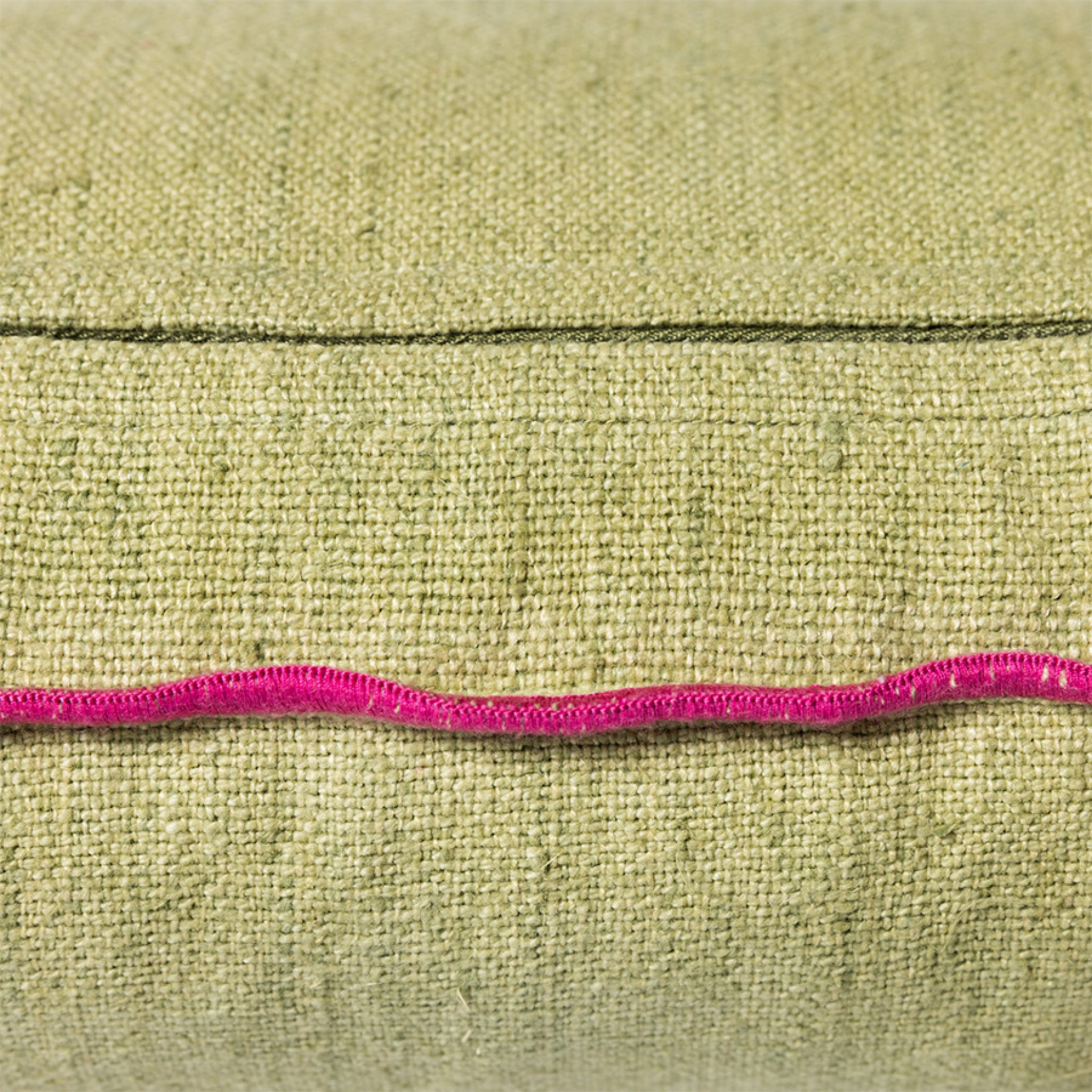 De HK Living Kussen Mansion Lichtgroen 50/30 heeft stof met textuur, een zichtbare naad en een golvende, felroze draad die horizontaal over het midden loopt.