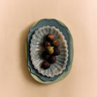 Een tros vijgen rust op een metalen bord met schulprand, gestapeld op decoratieve borden, waaronder de HK Living New Classics Resin Schaal Lichtblauw van HK Living, tegen een beige achtergrond.