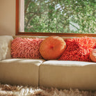 Een crèmekleurige HK Living bank met een Ripple Rond Kussen Sienna D50 kussen van HK Living staat bij een groot raam met groene bomen, het zonlicht stroomt naar binnen om een gezellige, uitnodigende sfeer te creëren.