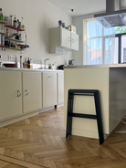 Moderne keuken met lichte kasten, een houten visgraatvloer, een strakke Hasegawa Lucano Ladder 2 Step Zwart van Hasegawa die tegen het kookeiland leunt, aan de muur bevestigde planken geïnspireerd op Japans design, en een groot raam dat natuurlijk licht binnenlaat.
