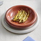 Een klein stapeltje ingemaakte gele chilipepers ligt in een Hay Barro Diepe Borden Terracotta D20 kom, op een wit bord boven een wit tafelkleed.