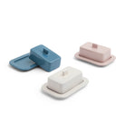 Drie rechthoekige boterschaaltjes van keramiek in blauw, wit en de Hay Barro Boterschaal Roze van Hay, elk met bijpassende deksels en bakjes, staan op een witte achtergrond. Het deksel van het blauwe boterschaaltje staat op een kier op het dienblad.