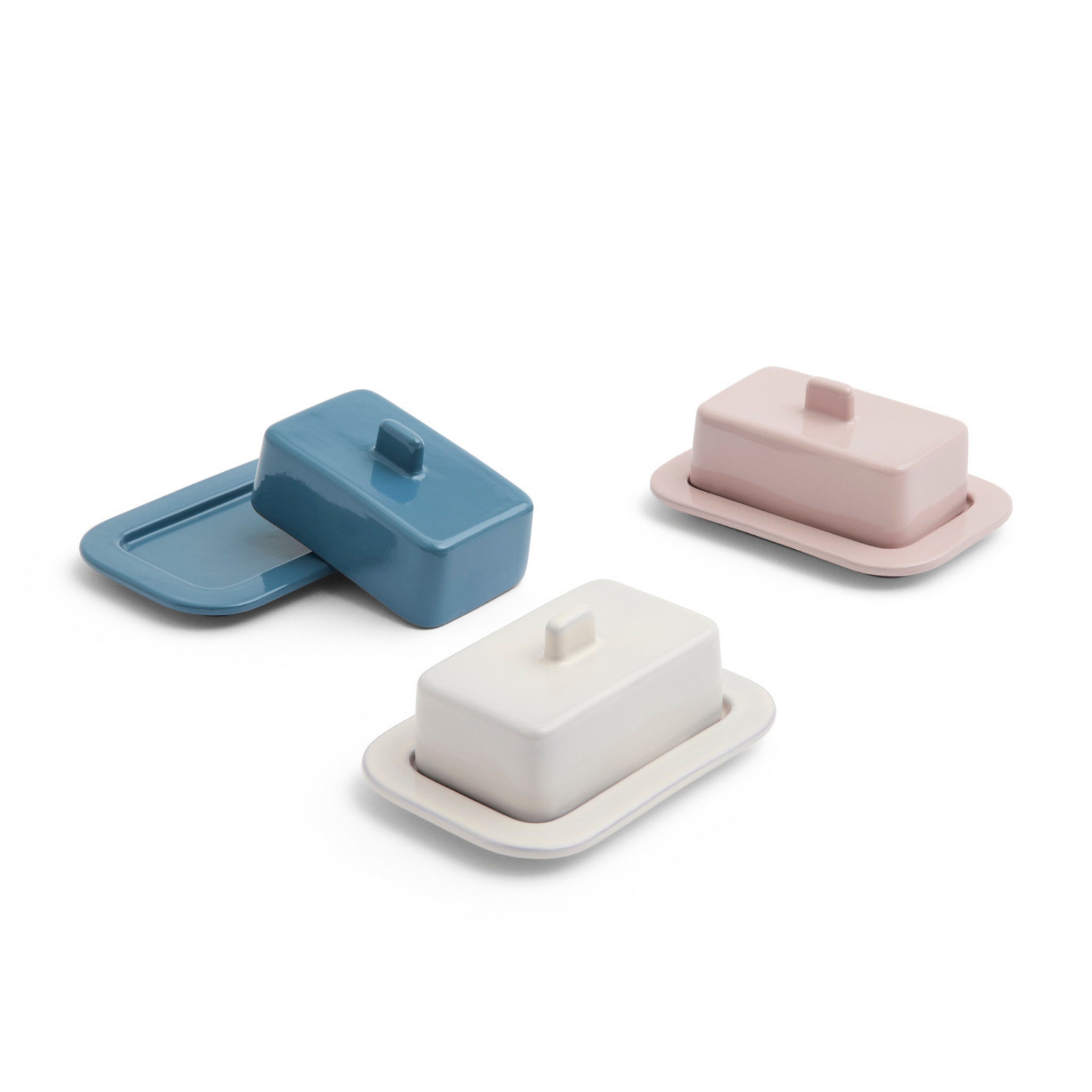 Drie rechthoekige boterschaaltjes van keramiek in blauw, wit en de Hay Barro Boterschaal Roze van Hay, elk met bijpassende deksels en bakjes, staan op een witte achtergrond. Het deksel van het blauwe boterschaaltje staat op een kier op het dienblad.