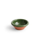 De Hay Barro Kom Groen D21 van Hay heeft een klein, rond terracotta ontwerp met een glanzende donkergroene binnenkant en rand, gecontrasteerd door een matte terracotta buitenkant, die doet denken aan Portugees servies, op een effen witte achtergrond.