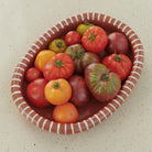 De Hay Barro Ovale Schaal Terracotta 27/36 van Hay heeft witte accenten en een mix van levendige heirloom tomaten - rood, oranje, groen en paars - op het licht gespikkelde oppervlak.