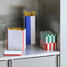 Een aanrecht met een glas water, ongekookte spaghetti, een open pastabak en twee gestapelde Hay Blikken Doos Blauw Off-White Slim voorraadblikken voegt een vleugje Scandinavisch design toe aan het roestvrij stalen oppervlak.