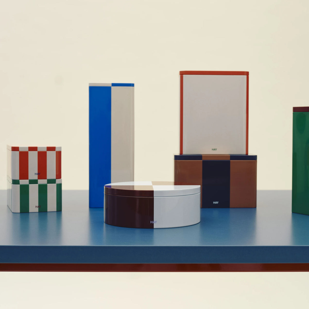 Een reeks Hay Blikken Dozen op een blauwe tafel, met vooraan de Hay Blikken Doos Bordeaux Ijsblauw Rond.