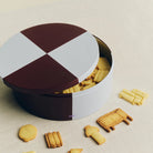Bovenaanzicht van de geopende Hay Blikken Doos Bordeaux Ijsblauw Rond vol koekjes, met koekjes verspreid op tafel.