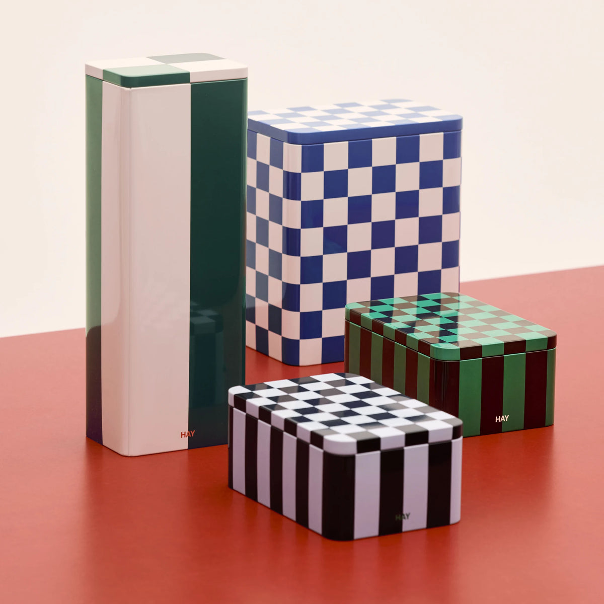 De Hay Blikken Doos Groen Off-White Slim staat rechtop op een rode tafel, samen met geblokte blikken dozen in blauw, groen en zwart.
