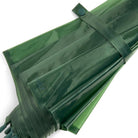 Close-up van de Hay Canopy Paraplu Groen van Hay, gevouwen en vastgezet met een bijpassende riem en drukknoop. Deze duurzame paraplu is gemaakt van gerecycled materiaal en heeft een waterafstotend scherm met een subtiele glanzende afwerking.