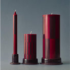 Drie Hay Zuil Kaars Wijn Bordeaux H15 van Hay, elk met glanzende ruitmotieven, staan rechtop op bijpassende donkere houders tegen een neutrale grijze achtergrond - ideaal voor een modern interieur.