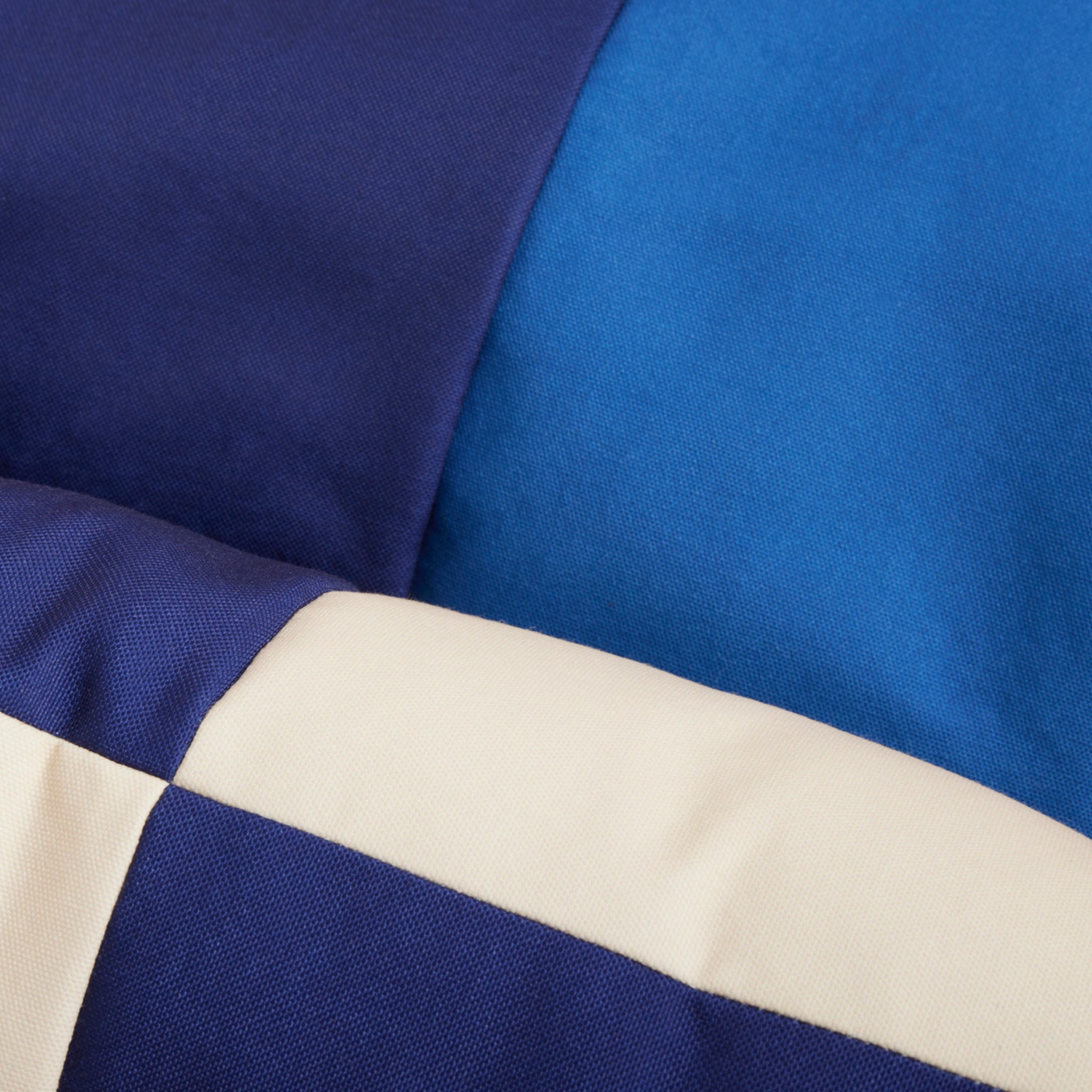 Close-up van een stoffen quilt met gedurfde, vierkante delen in navy en crème, die het ontwerp van de Hay Dogs Hondenmand Rood Blauw 65/78 van Hay nabootsen. Het stiksel en de textuur zijn duidelijk zichtbaar.