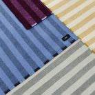 Bovenaanzicht van uitgespreide Hay Duo Plaids met brede strepen, met de Hay Duo Plaid Hemelsblauw centraal tussen pruim, geel en grijs.