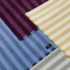 Bovenaanzicht van uitgespreide Hay Duo Plaids met brede strepen, met de Hay Duo Plaid Pruim bovenaan naast hemelsblauw, geel en grijs.