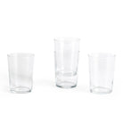 Vier heldere Hay Glas Helder L tumblers van Hay staan op een witte achtergrond. Twee glazen zijn gestapeld en de andere twee staan los van elkaar, waardoor hun minimalistische ontwerp en stapelbare vorm goed tot zijn recht komt.