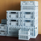 Een stapeltje Hay Kleur Krat Mini Lichtblauw opbergkratten van gerecycled plastic van het merk Hay staan in verschillende maten op een donkerbruin oppervlak tegen een houten achtergrond.