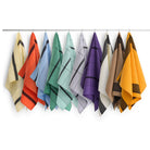 Een rij kleurrijke handdoeken, waaronder de Hay Linear Theedoek Hemelsblauw van Hay, hangt netjes aan een stang tegen een witte achtergrond. De handdoeken zijn gerangschikt in geel, oranje, rood, groen, blauw, paars, bruin en goud.