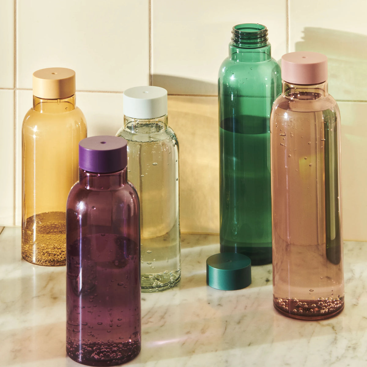 Hay Miz waterflessen op een marmeren aanrecht tegen witte tegels, met rechts de Hay Miz Waterfles Mauve 720 ml met roze dop.