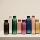 Een rij Hay Miz waterflessen in verschillende kleuren en maten op een witte sokkel, waaronder de Hay Miz Waterfles Rood 540 ml.