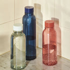 De Hay Miz Waterfles Rood 540 ml op een marmeren aanrecht in het zonlicht, naast een heldere en een donkerblauwe Miz waterfles.