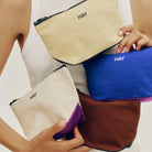 Een persoon in een witte tanktop houdt vier Hay opbergzakjes vast, waaronder het Hay Multi Opbergzakje Geel S, elk met "HAY" in zwarte letters voor een kenmerkend Scandinavisch tintje.