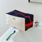 Een Hay Multi Toilettas Medium Crème van Hay, gemaakt van biologisch katoen met navy, crème, bruine en rode kleuren en een rode rits, staat op een witte wastafel. Voorop staat een blauwe tandenborstel met een groen handvat.