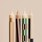 Vier hoge Hay Patroon Kaarsen Crème en Donker (set van 4) van het merk Hay, met geometrische patronen in beige, zwart, groen en bruin tegen een neutrale achtergrond-stijlvol als decoratie of geschenk.