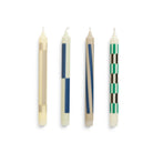 De Hay Patroon Kaarsen Crème en Donker 4 st. van Hay heeft vier rechtopstaande witte kaarsen, elk met unieke geometrische patronen in beige, blauw, bruin en groen - ideaal voor cadeauverpakkingen.