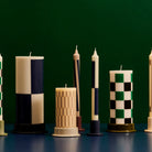 De Hay Patroon Kaarsen Crème en Donker 4 st. van Hay heeft decoratieve kaarsen met marineblauwe, groene, beige en witte geometrische patronen op een donkergroene basis, gerangschikt in houders en verpakt als een perfect cadeau.