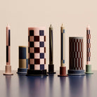 De Hay Patroon Kaarsen Roze en Blauw 4 st. van Hay heeft vier decoratieve kaarsen met geometrische patronen in roze en blauw, perfect als stijlvol cadeau en ideaal om te presenteren op kleurrijke houders tegen een neutrale achtergrond.