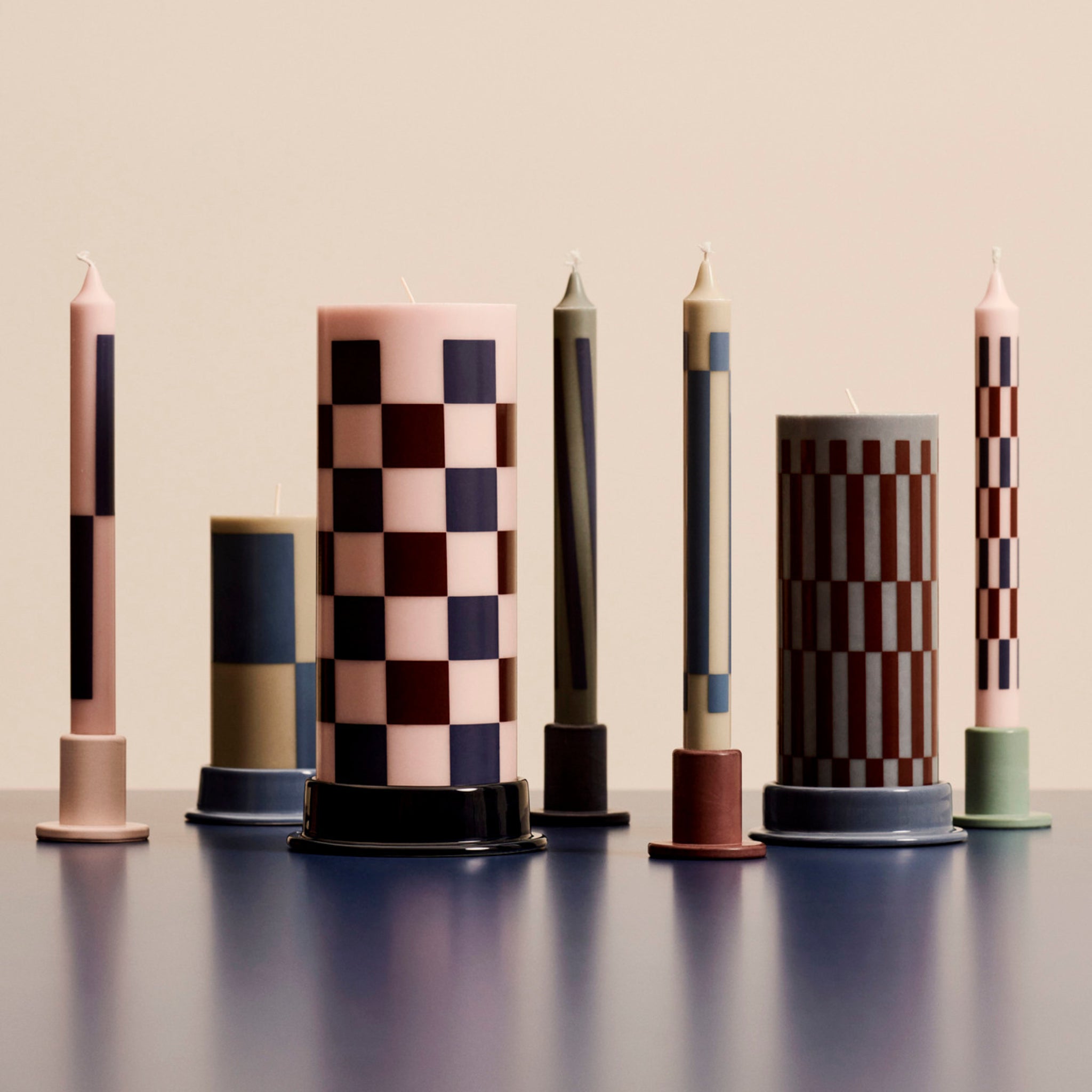 De Hay Patroon Kaarsen Roze en Blauw 4 st. van Hay heeft vier decoratieve kaarsen met geometrische patronen in roze en blauw, perfect als stijlvol cadeau en ideaal om te presenteren op kleurrijke houders tegen een neutrale achtergrond.