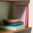 Een Hay Slice Snijplank Groen 20/30 ligt op een houten plank, gestapeld met roomkleurige en koraalkleurige snijplanken. Bruine en blauwe theedoeken liggen opgevouwen bovenop en een roze middelgrote snijplank staat er rechtop achter.