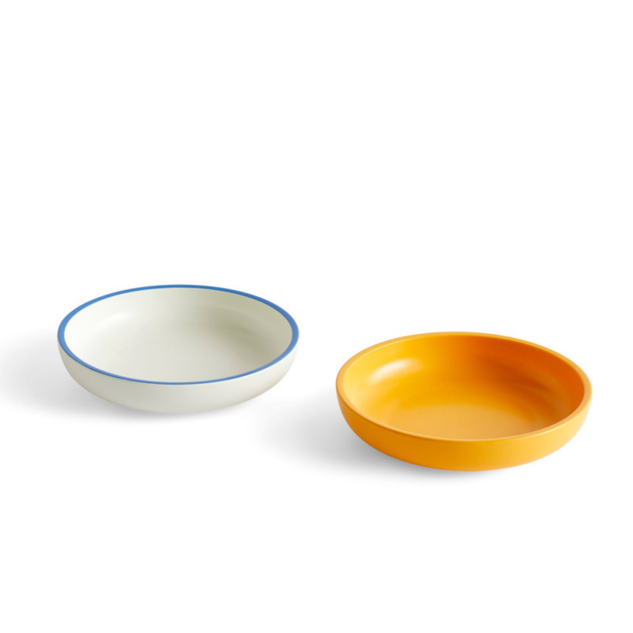 Twee ronde, ondiepe kommen op een witte achtergrond; de ene is wit met een blauwe rand en de andere is de Hay Sobremesa Serveerschaal Geel D25 van Hay.