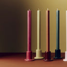 Een rij Hay Tube Kandelaars met lange kaarsen op een terracotta tafel, met vooraan links de Hay Tube Kandelaar Bessenroze.