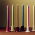 Een rij Hay Tube Kandelaars met lange kaarsen op een terracotta tafel, met in het midden de Hay Tube Kandelaar Kastanjebruin.
