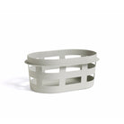 De Hay Wasmand Lichtgrijs van Hay is een ovale, lichtgrijze mand met open rechthoekige uitsparingen, gemaakt van gerecycled polypropyleen en afgebeeld op een effen witte achtergrond.