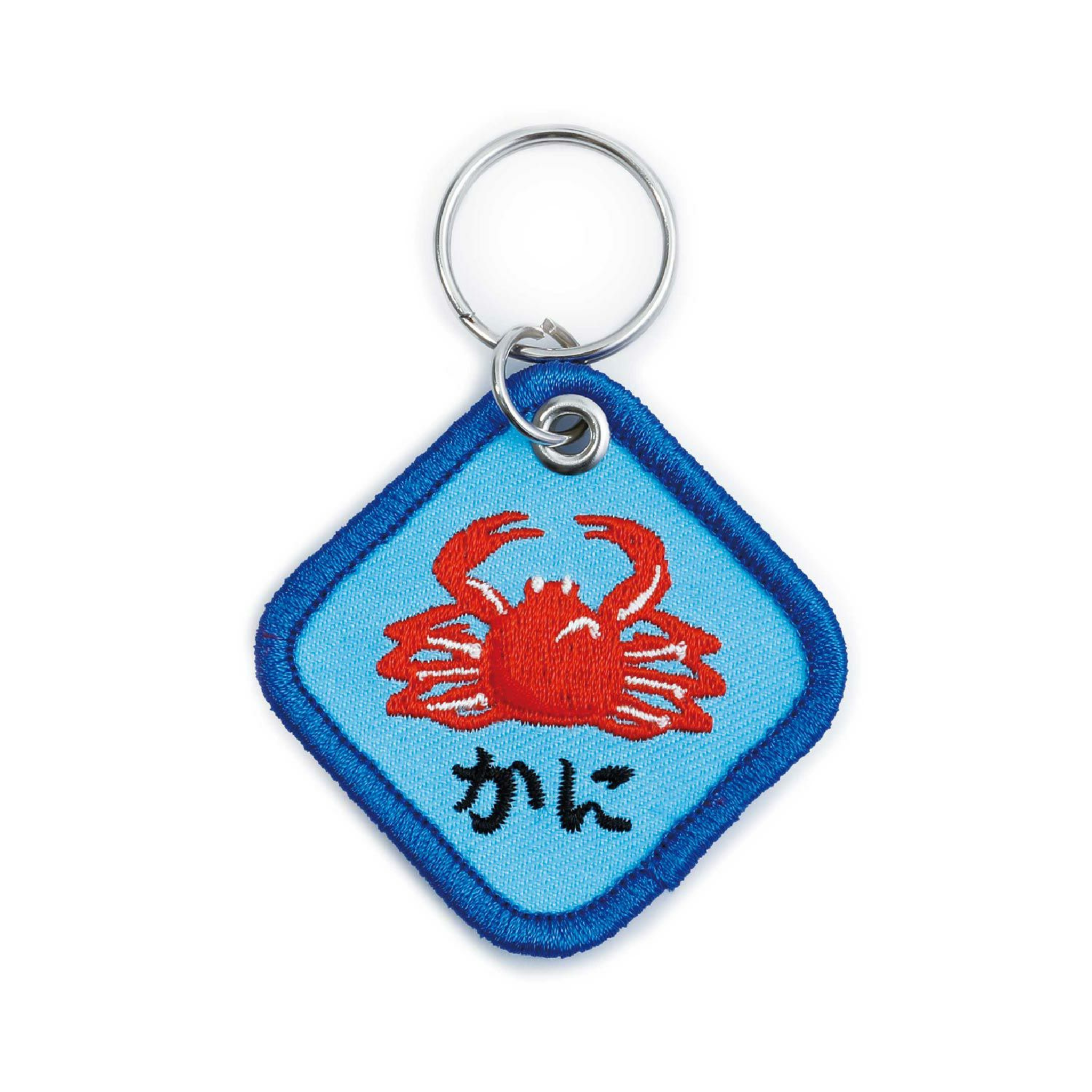 De Hightide Stitch Work Sleutelhanger Krab is een blauwe, diamantvormige sleutelhanger van Hightide, met een rood geborduurde krab en Japanse tekst, bevestigd aan een zilveren sleutelhanger - een speels accessoire voor je sleutels.