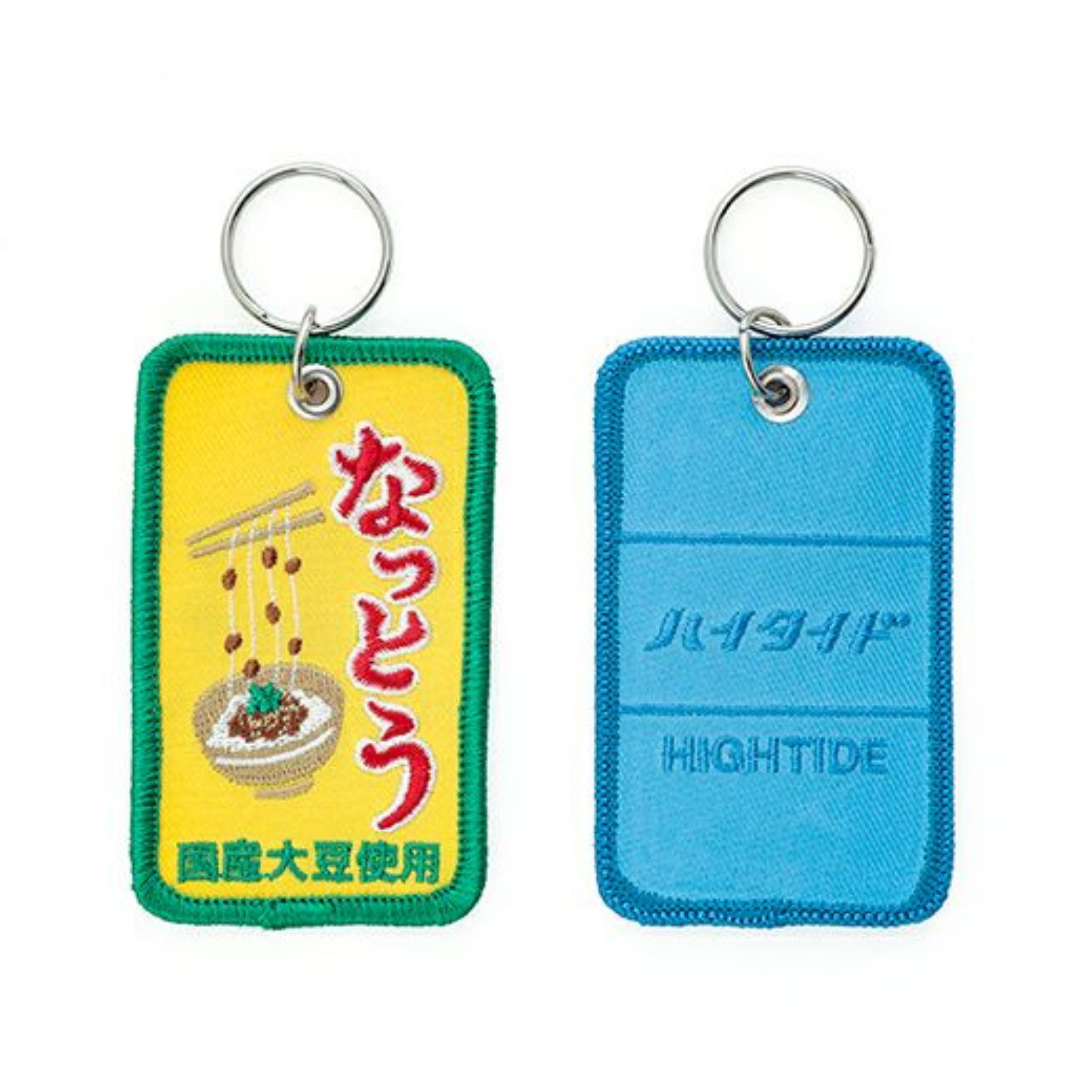 Twee rechthoekige sleutelhangers: een gele Hightide Stitch Work Sleutelhanger Natto met groene bies en geborduurde nattokom, en een blauwe Hightide sleutelhanger met bijpassende bies - beide met Japanse tekst.