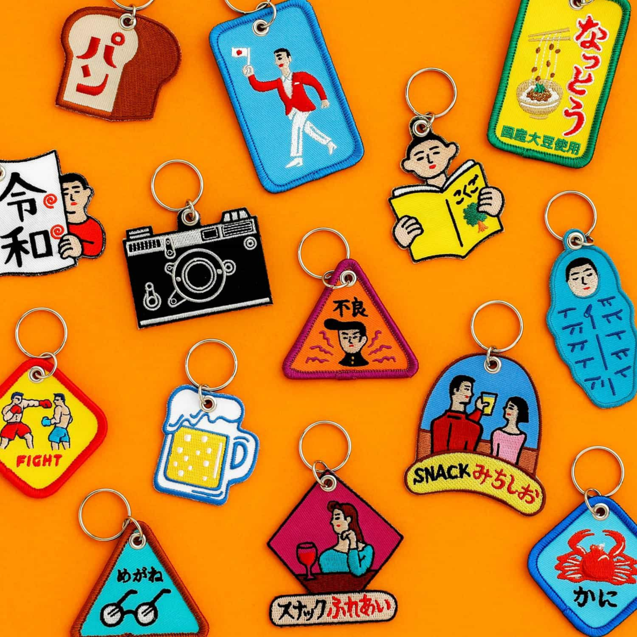 Hightide Stitch Work Sleutelhanger Brood van Hightide is een kleurrijke sleutelhanger met Japanse illustraties en tekst in cartoonstijl, met toast tussen speelse ontwerpen tegen een feloranje achtergrond.