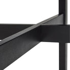 Close-up van kruisende zwarte balken van het Hubsch Fjord Eettafel Essenhout Zwart D120 frame, tegen een witte achtergrond.