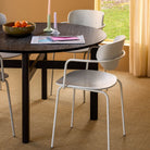 De Hubsch Fjord Eettafel Essenhout Zwart D120 van Hubsch, in combinatie met witte stoelen, een schaal sinaasappels, kaarsen en tijdschriften, staat op beige tapijt in een zonnige kamer met gele muren en crèmekleurige gordijnen.