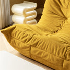 Een close-up van een mosterdgele, getufte loungestoel naast de &Klevering Whip Pillar Bijzettafeltje Gebroken Wit, een sculpturale en duurzame bijzettafel van glasvezel, in een gezellige kamer met houten vloeren en neutrale muren.