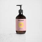 Een bruine pompflacon van Matriks Fragrances Hand & Body Wash Citrus & Grapefruit 490 ml met een roze label en gele cirkel staat op wit marmer, met een veganistische formule en verfrissende grapefruitgeur tegen een effen witte achtergrond.
