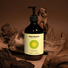 Een bruine fles Matriks Fragrances Hand & Body Wash Ginger & Cardamom 490 ml rust tussen het drijfhout, met een geelgroen etiket - en brengt unieke geuren naar je handzeeproutine met zijn veganistische gember- en kardemomgeur.